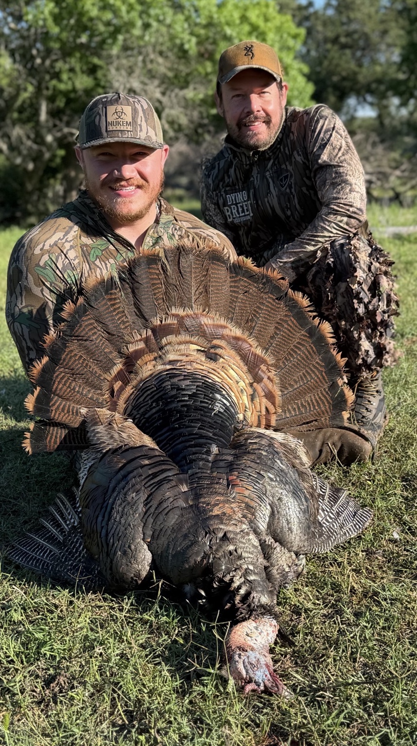 Two hunters posing with a turkey in the field